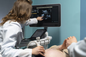 Gestante em consulta médica com profissional da saúde mostrando imagem de ultrassom em tela, em ambiente acolhedor e calmo.
